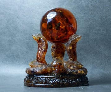 3 Baltische amber-kobras die een amberbal vasthouden. -