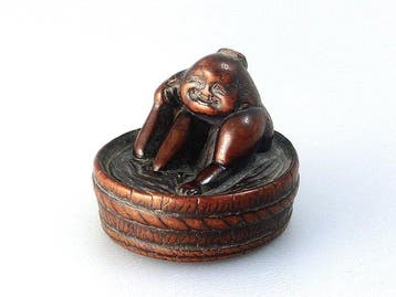 Charmant netsuke waarop Okame een bad neemt in een brede