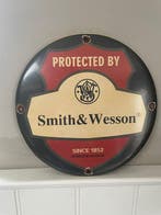 Emaille reclamebord – Smith & Wesson – “Protected by” – rond, Antiek en Kunst, Antiek | Wandborden en Tegels