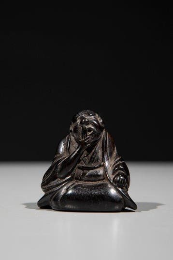Een houten netsuke van een knielende man die aan zijn baard