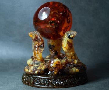 3 Baltische amber-kobras die een amberbal vasthouden. -